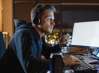 Side view serene unshaven man listening music while drinking mug of beverage. He looking at screen of computer. Job concept