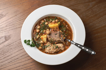 Lamb soup of red lentils, celery and greens, on a wooden table.