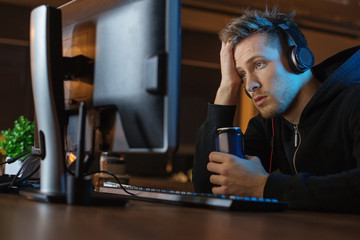 Portrait of weary bearded male hearing song while looking at computer. He drinking alcohol beverage. Rest and fatigue concept