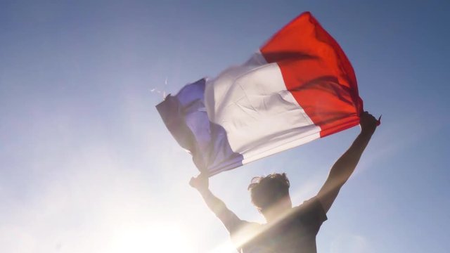 Young man holding french national flag to the sky with two hands at the beach at sunset france