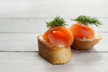 Salmon sandwiches on white wooden board with black olives and herbs.Buffet food, healthy sandwiches