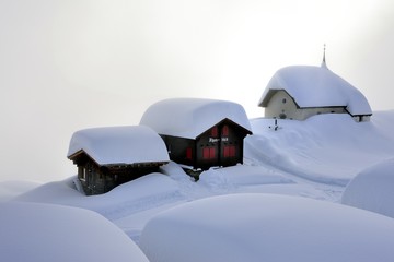 Verschneite Kapelle mit Holzhütten auf Bettmeralp im Nebel