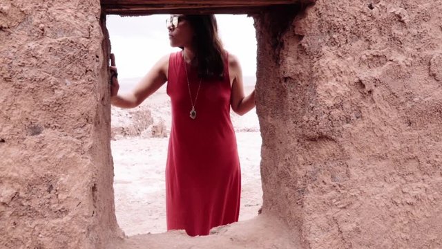 Hispanic model posing behind window of an Adobe house.