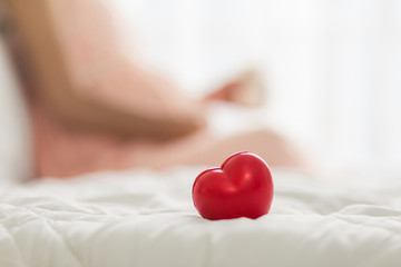 Red heart on the bed, Blurred background of pregnancy woman  in pink dress  in bedroom.