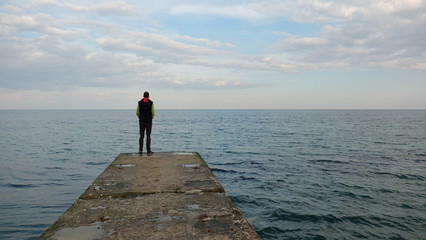 A young man stands at the pier and looks at the distance.