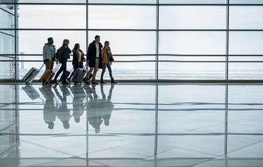 Travel together. Full length of pleasant young men and women are walking along terminal hall with...