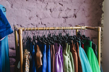 A stand with hangers with colorful clothes on the background of a textured brick wall of purple