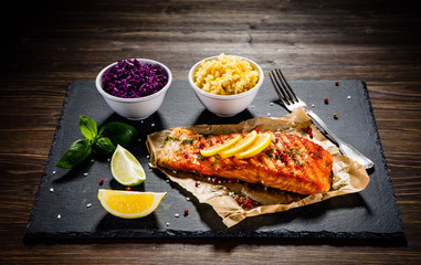 Grilled salmon with vegetables served on black stone plate on wooden table 
