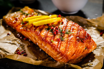 Grilled salmon with vegetables served on black stone plate on wooden table  - obrazy, fototapety, plakaty