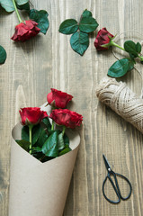 Fototapeta premium Florist making a red roses bouquet, wrapping in kraft paper on a wooden table. View from above.