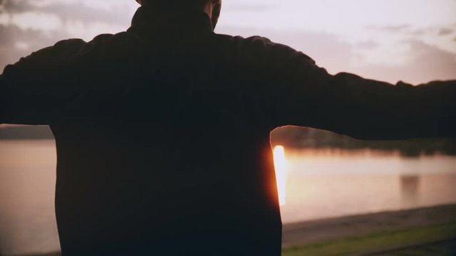 4K Sportsman exercising near sunrise morning lake. Back view male swinging arms and jumping. Professional fit athlete.