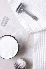 Safety razor with towel, brush and soap and blade on a gray tile surface