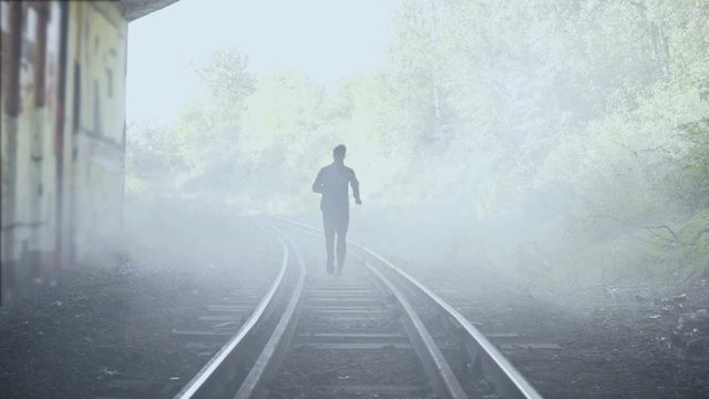 4K Man running away fast on foggy train tracks. Back view. Abstract background shot. Creative lifestyle runner shot.
