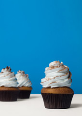 three cupcakes with white cream, sprinkled with cocoa on a white table on a blue background