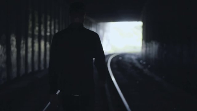 4K Concept of depression. Dark man silhouette. Back view. Abstract cinematic shot. Male walking in a railway tunnel.