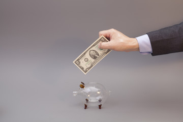 Businessman putting two dollar bill into glass piggy bank