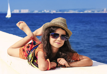 A girl in bright clothes and a straw hat lies and rests on the beach on the pier