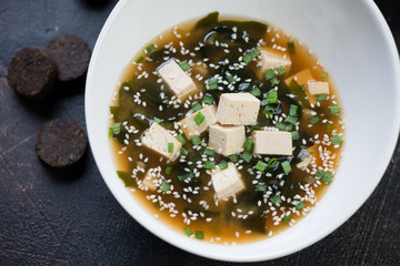 Close-up of miso soup with tofu cheese, wakame seaweed, sesame and green onion served in a white bowl