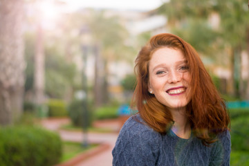 Portrait of a natural girl, without retouching, with healthy skin. The woman is smiling. Red-haired girl with freckles posing near palm trees
