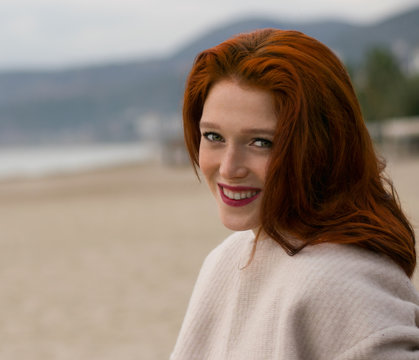 A nice  girl with a beautiful smile is sitting on the beach. A woman with red hair and freckles. Vacation lifestyle