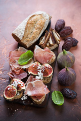 Bruschettas with prosciutto ham, ripe figs and date fruits, rusty metal background, studio shot