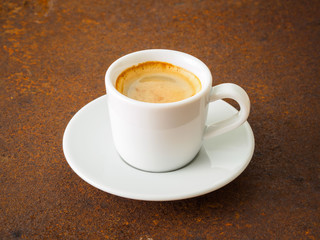 black frothy coffee with foam in white cup with plate on  rusty metal table, side view