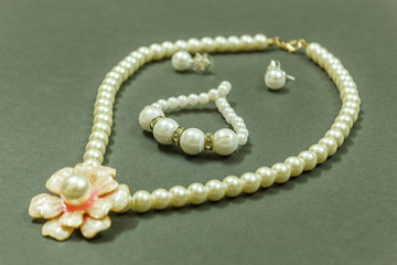 Showcase of Ivory colored gem necklace with flower shaped pendant, bracelet and earrings in a dark background. With selective focus on the subject.