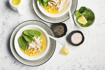 Fresh homemade chicken soup broth with corn, spinach, boiled breast on a light background. Top view. Copy space.