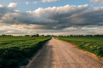 Fototapeta na wymiar Gravel road to home in country at sunset with cloudy sky
