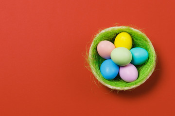 Fototapeta na wymiar Six colorful pastel monophonic painted Easter eggs in basket with green grass isolated on red background. Happy Easter concept. Copy space for advertisement. With place for text. Top view on eggs.