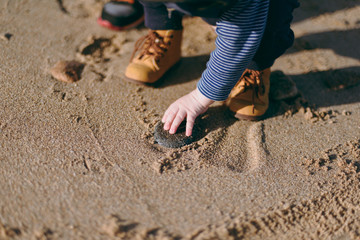 Close up of legs kid boy in yellow boots on sand of sea sunny beach. Child little feet walking on nature, hand touching ocean sand. Parenthood, family day 15 of may, love parents, children concept.