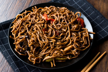 Noodle with Soy Sauce Served with Chopsticks and Black Plate on Dark Wooden Surface.