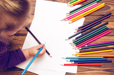 Naklejka premium Little girl draws with pencils on a wooden table