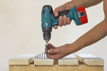 Hand of a worker screws a screw in a wooden board with a cordless screwdriver. Man carpenter at...