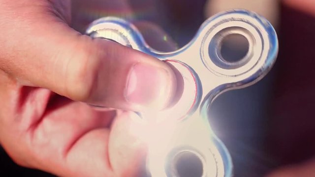 Close up of man's hand is held by a spinning spinner in slow motion. The silver spinner reflects the rays of the sun. 1920x1080