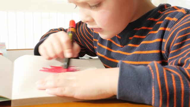 A dolly shot of a boy coloring on paper at a table in the house