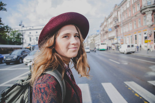Lifestyle portrait of young cute hipster woman in a hat walking on the street