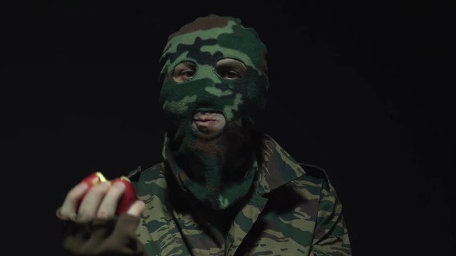 Soldier in camouflage and military mask eating red apple over black background
