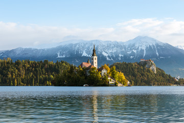 The sun rises above Lake Bled on a clear day. The mountains are visible behind the church on the island at Lake Bled.