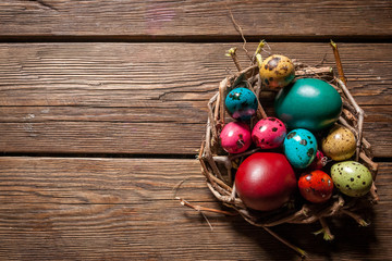 colored chicken and quail eggs in a small nest on wooden background for Holy festival of Easter