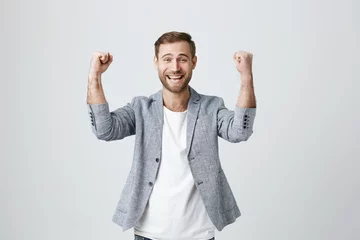 Foto op Plexiglas Happy lucky overjoyed male winner with stubble in trendy clothes clenches fists, rejoices triumph at work, glad to recieve high profits, has own prosperous business. Good-looking guy achieves goals © Cookie Studio