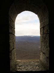 old stone window in the form of an arch with a view of the mountains