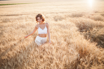 Naklejka na ściany i meble Woman in a wheat field on a summer sunset in white