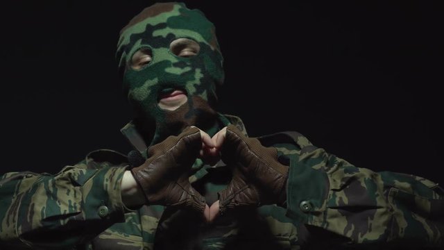 Soldier in camouflage and a military mask making a heart with hands, isolated on black
