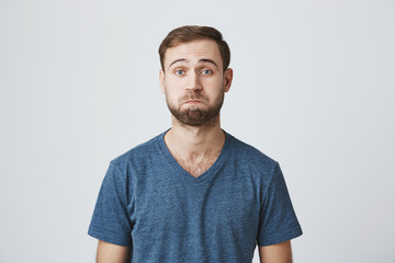 Unhappy gloomy bearded attractive male curves lips has sorrorful expression as doesn`t understand what is going on, feels depressed and frustrated, expresses negative emotions. People and emotions