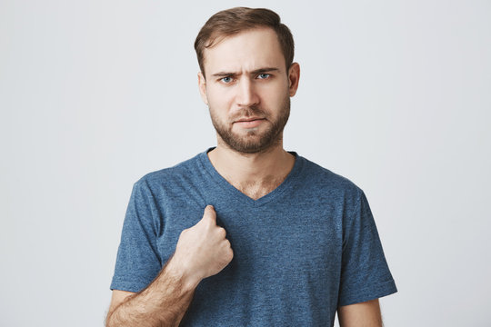 Displeased frustrated man with stubble points with forefinger at himself, can`t understand something, frowns his face, looks angrily at camera. Negative emotions, feelings, and reaction.