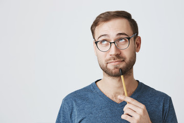 Pensive bearded university professor in spectacles with clever expression looks thoughtfully aside,...