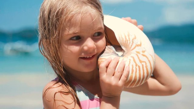 Cute little girl playing with huge sea shell on beach