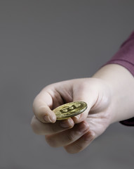 An isolated image of a hand holding/flipping a bitcoin on a grey background. Bitcoin is a crypto currency and a worldwide payment system. 