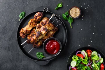 Wall murals meal dishes Grilled meat skewers, shish kebab and healthy vegetable salad of fresh tomato, cucumber, onion, spinach, lettuce and sesame on black background, top view